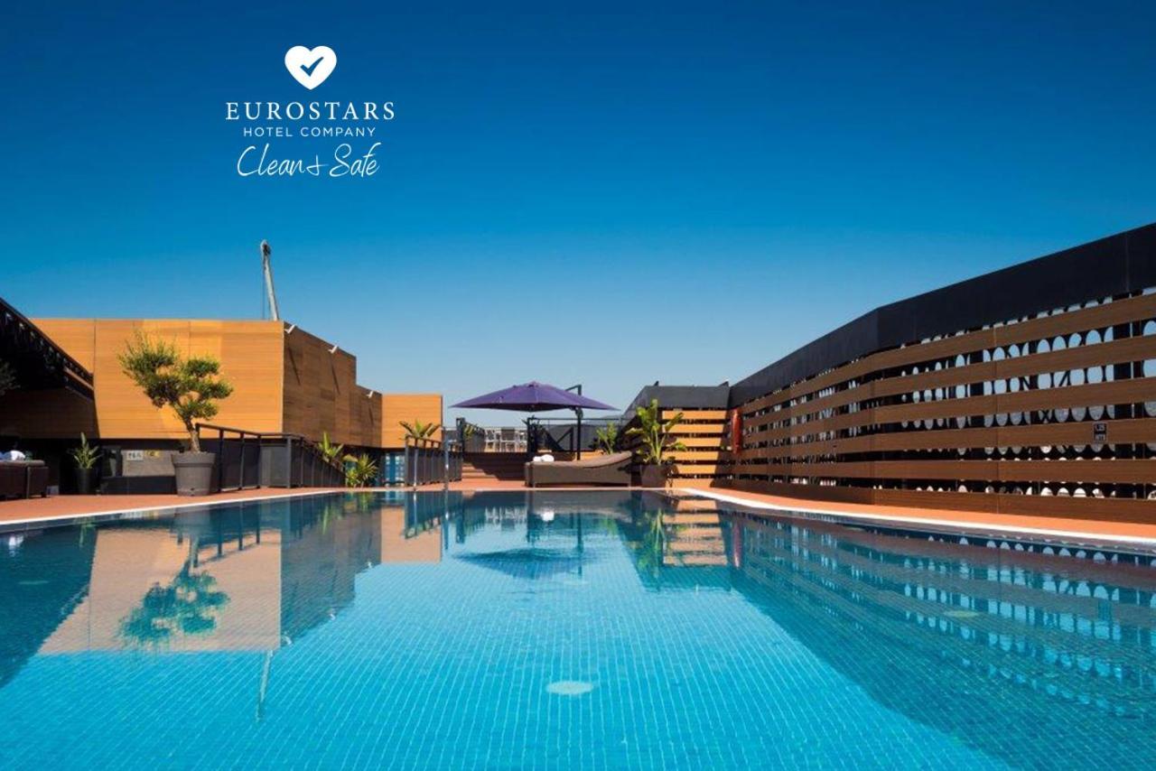 Eurostars Palace Córdoba Exterior foto The photo shows an outdoor swimming pool with clear, blue water, reflecting the blue sky above. The pool area is surrounded by modern architectural features, including wooden slats and potted plants. There is also a purple umbrella providing shade. T
