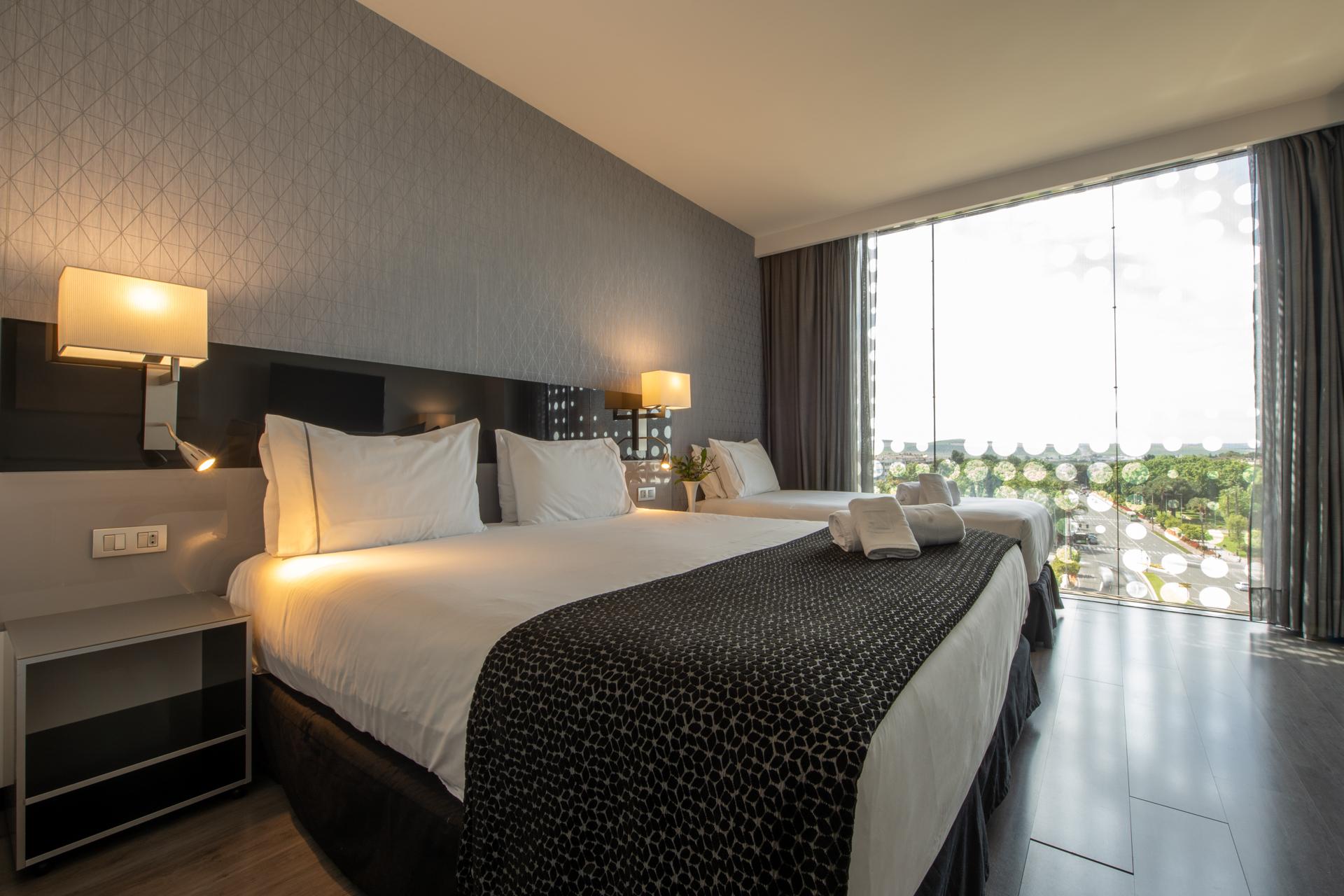 Eurostars Palace Córdoba Exterior foto The photo shows a modern hotel room featuring two large beds with white linens and dark patterned bedspreads. Each bed has a set of pillows and a decorative cushion. There are bedside lamps on either side of the beds, and a contemporary piece of furn