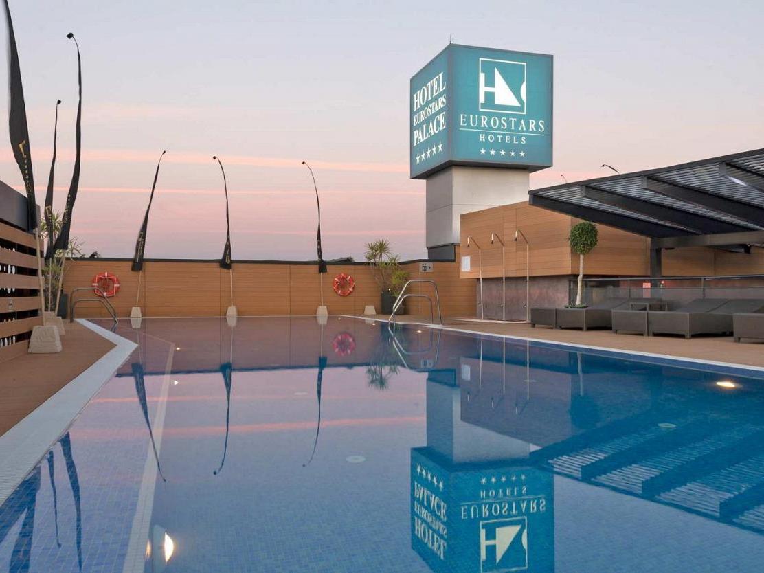 Eurostars Palace Córdoba Exterior foto The image shows a hotel pool area at twilight. The pool is large and reflective, capturing the colors of the sky and surrounding features. In the background, there is a hotel sign displaying the Eurostars brand, with a modern architecture style. The 