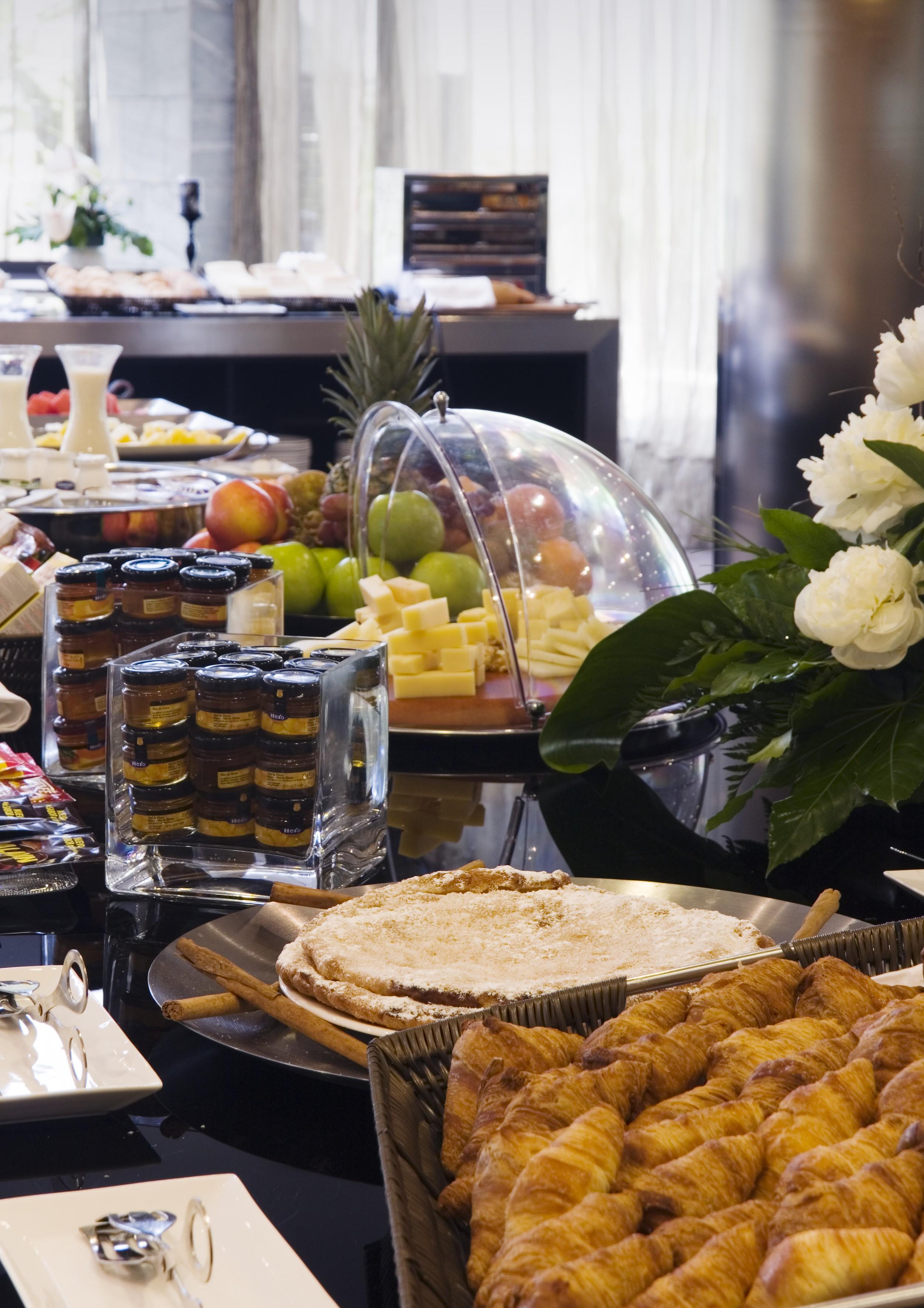 Eurostars Palace Córdoba Exterior foto The photo shows a buffet-style arrangement with a variety of food items. There are fruits such as apples and grapes displayed prominently, along with a selection of cheeses presented on a wooden platter. A glass dome covers some of the items, possibl