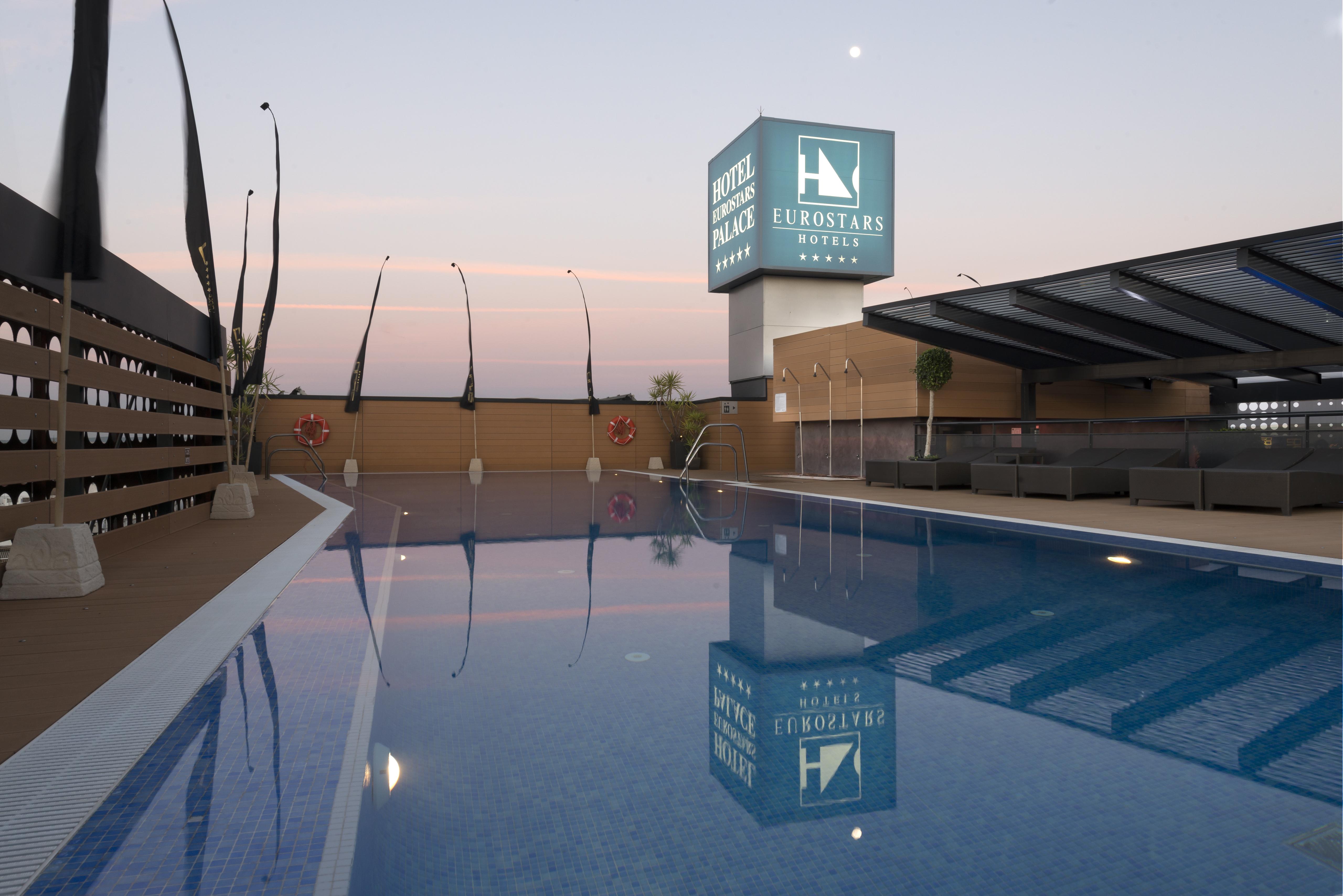 Eurostars Palace Córdoba Exterior foto The photo shows a rooftop space featuring a swimming pool. The pool has a clear blue water, and the area around it is designed with modern aesthetics, including a wooden deck and comfortable seating. In the background, there is a prominent sign for "