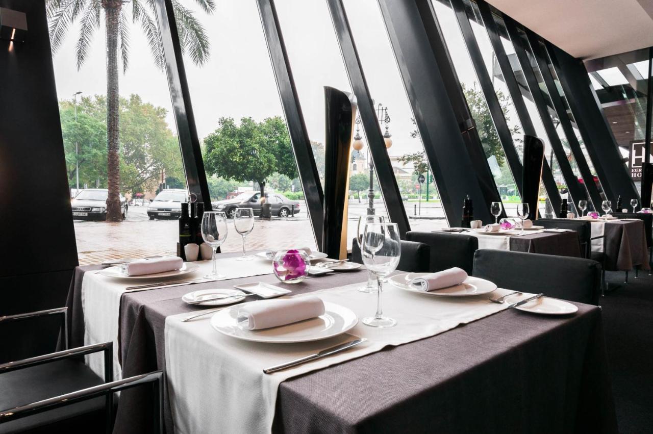 Eurostars Palace Córdoba Exterior foto The photo shows an elegant restaurant interior with large windows featuring modern angular designs. There are two dining tables set up, each covered with white and dark tablecloths. The tables are elegantly arranged with plates, cutlery, and wine gla